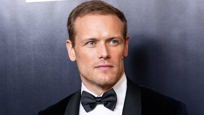 Sam Heughan in a tuxedo staring to his left