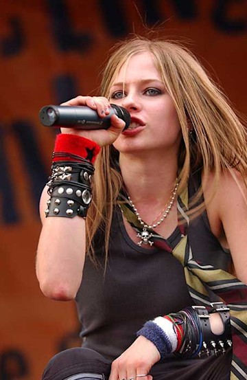 Avril Lavigne singing into a microphone while crouched on stage