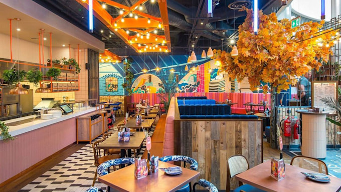 the colourful interior of a zizzi restaurant with orange foliage hanging from the ceiling and bright chairs around square tables