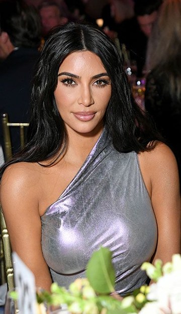 kim is seated wearing a tightly fitted one shoulder dress and she her long black hair is pushed back off her shoulders