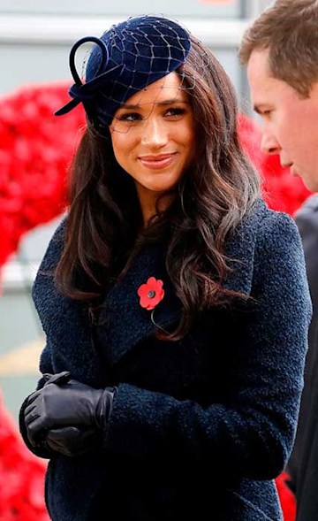 meghan smiles at a man who is speaking to her as she clasps her hands gently over her baby bump in an all navy winter ensemble