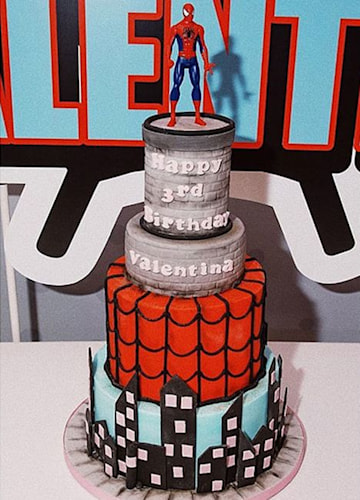 A 4-tier cake that looks like a city skyline and a 1-tier red and black cake that looks like a Spider-Man costume