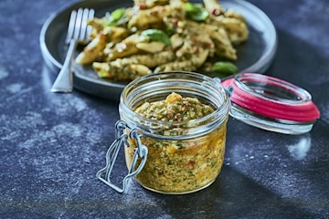 jar of green pesto next to plate of pasta