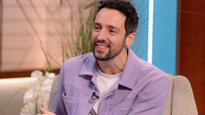Ralf Little wearing a lilac shirt and smiling. 