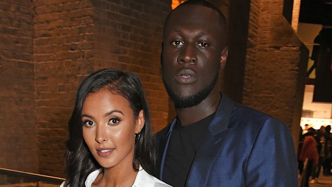 Close up photo of Maya Jama and Stormzy at an event together. She is wearing a white suit and he is wearing a navy suit. 