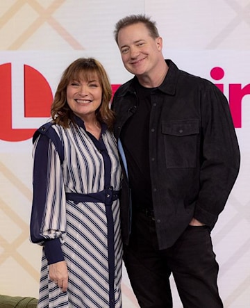 Brendan Fraser y Lorraine Kelly sonríen mientras posan juntos para una foto. 