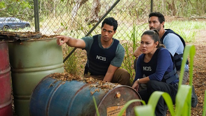 Alex Tarrant as Kai Holman, Vanessa Lachey as Jane Tennant, and Noah Mills as Jesse Boone. They're hiding by some barrels, spying on something ahead. 