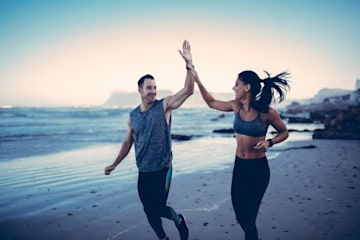 Man and woman high fiving running on the beach