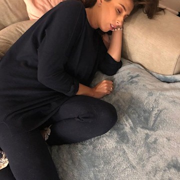 A close-up photo of Stacey curled up in black loungewear and sound asleep on a brightly colored sofa topped with a baby blue fluffy blanket