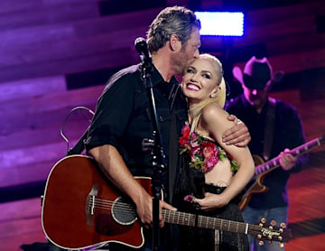 Blake Shelton holds guitar and hugs Gwen Stefani on stage