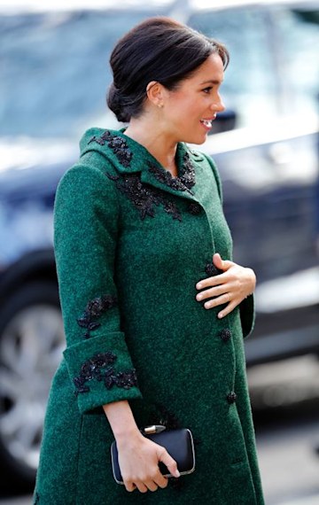 Meghan Markle wears a green coat and holds her pregnancy bump