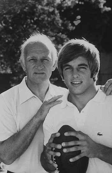 A teenaged Mark Harmon holding a football as he poses with father Tom.