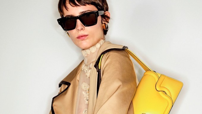 Woman wearing sunglasses, lace top, trench coat and yellow shoulder bag 