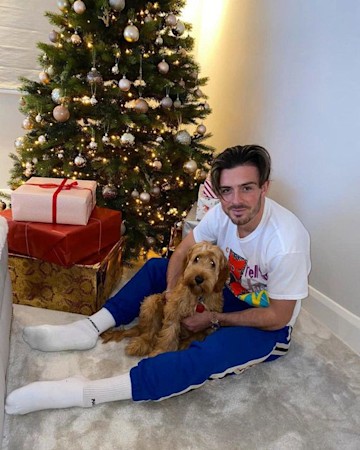 Jack Grealish cuddling his dog as he poses in front of Christmas tree