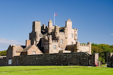 a castle in a field surrounded by a wall with a union jack flag flying above at full mast