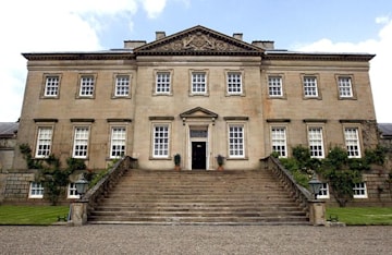 a huge rectangular brown grey stone house with a wide stone staircase leading to the narrow front door