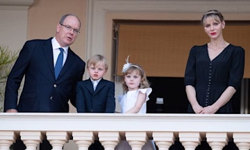 albert and charlene dresssed in formal navy attire on either side of a young boy and girl on a balcony stone balustrades