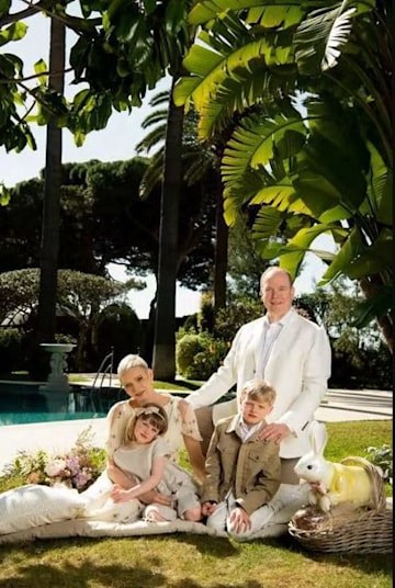 a family photo taken in a garden by a pool on a sunny day featuring a young boy girl mother and father sitting and kneeling together coordinated in pale clothing
