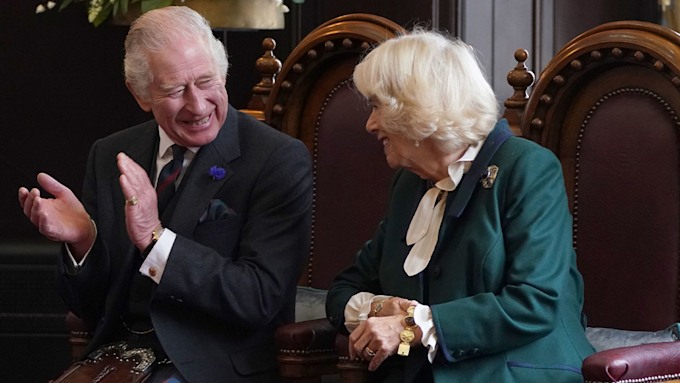king charles smiling on throne alongside wife camilla 