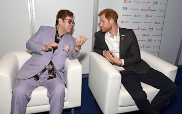 elton john leans in to talk to prince harry as they sit side by side on white chairs