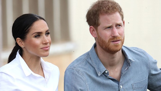 prince harry and meghan markle look concerned as they stand side by side