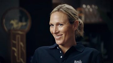 Zara Tindall smiles wearing a navy blue polo shirt