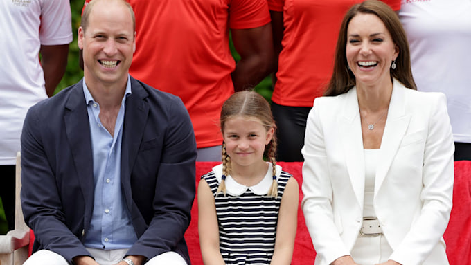 princess charlotte smiles as she sits inbetween her parents kate middleton and prince william