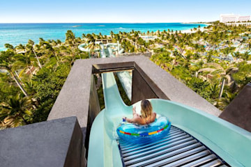 a view from the top of a towering water slide with a child about to to descend in a rubber ring and the ocean is in sight on the horizon