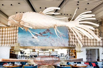 a wooden chandelier shaped like a tropical fish hangs from the wooden beams of a ceiling inside a restaurant 